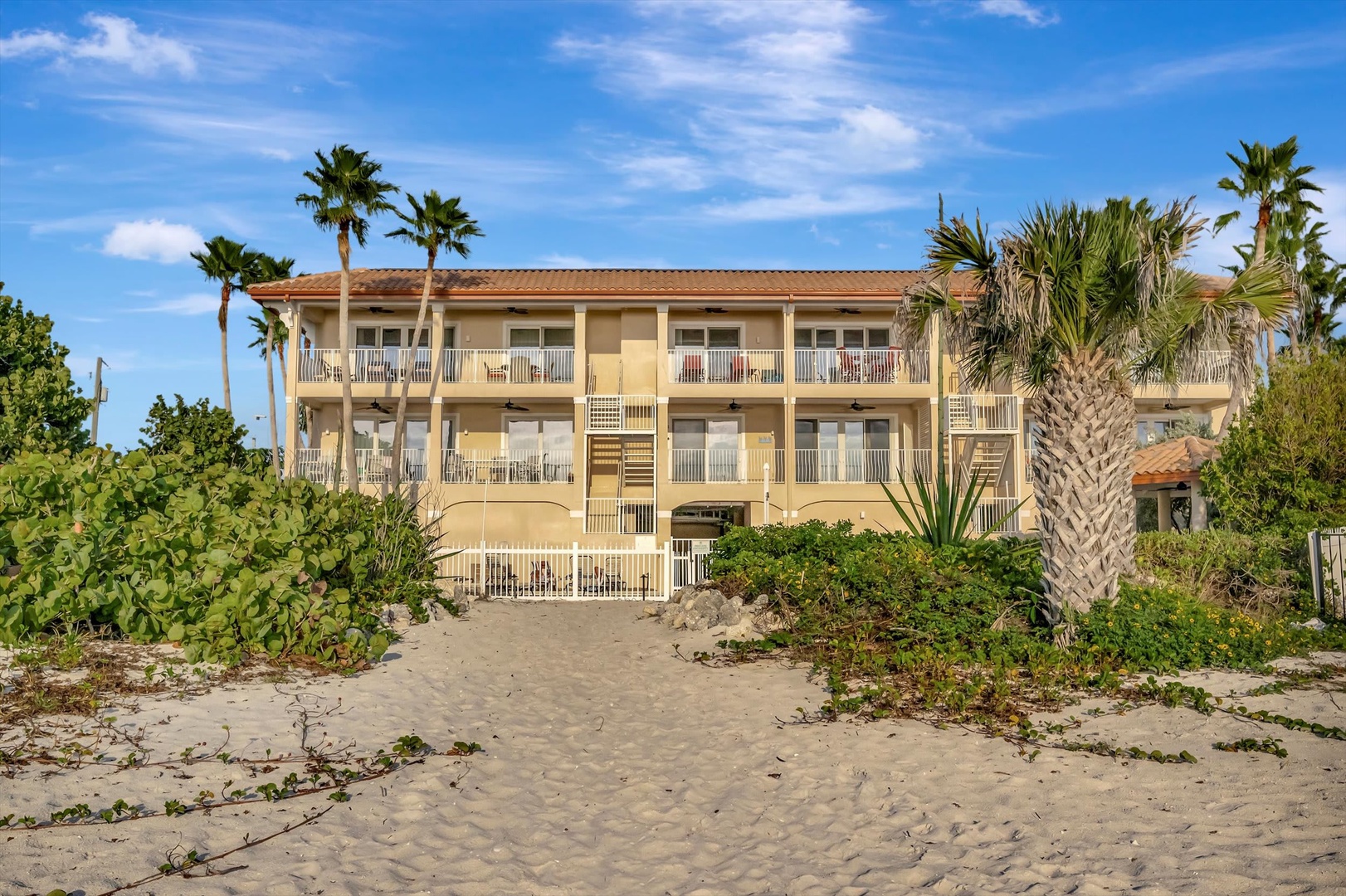 A beachfront property with balconies overlooking tropical palms and sandy shores, steps from the water.