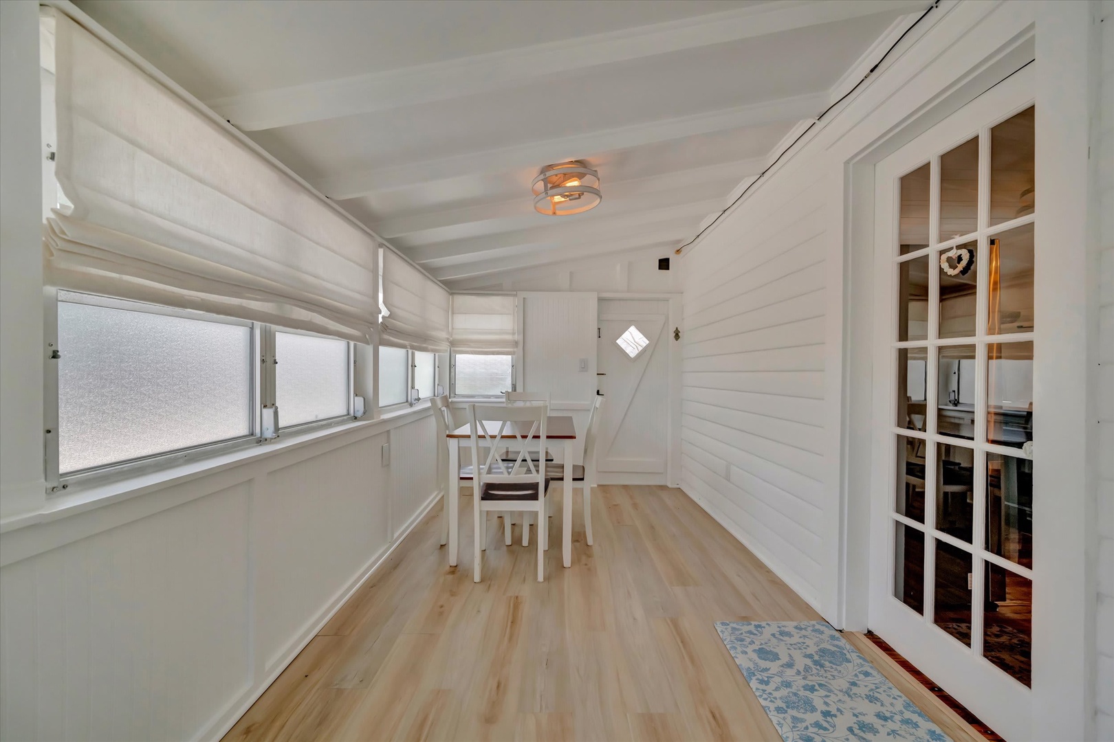 Bright, open dining space with light hardwood floors and shiplap walls creates a welcoming atmosphere for your morning coffee or evening meals. Warm ceiling fixture adds a cozy coastal charm.