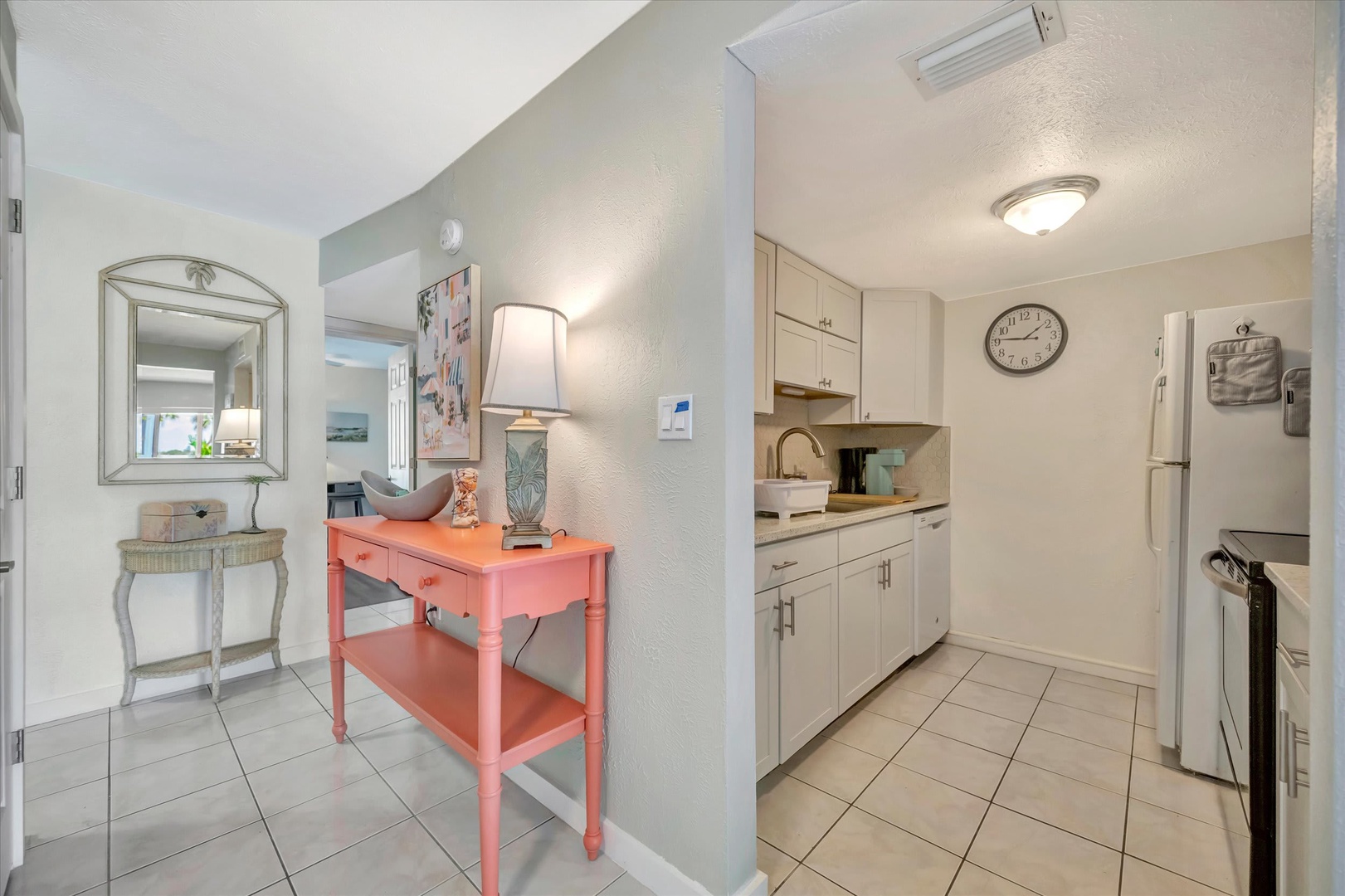 Your bright, cheerful entryway welcomes you with coastal charm—a pop of coral against soft beach tones, leading into your fully equipped kitchen where morning coffee awaits.