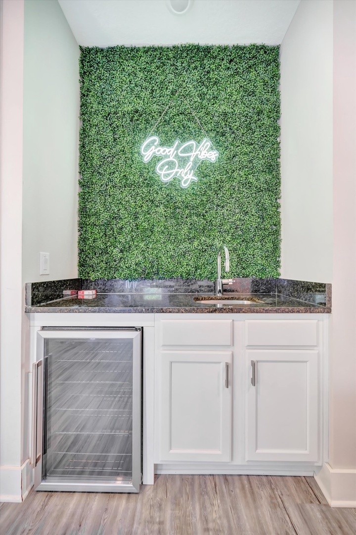 Pour yourself something refreshing at your own stylish wet bar, complete with a beverage cooler and a vibrant living wall backdrop that says it all: 'Good Vibes Only.'