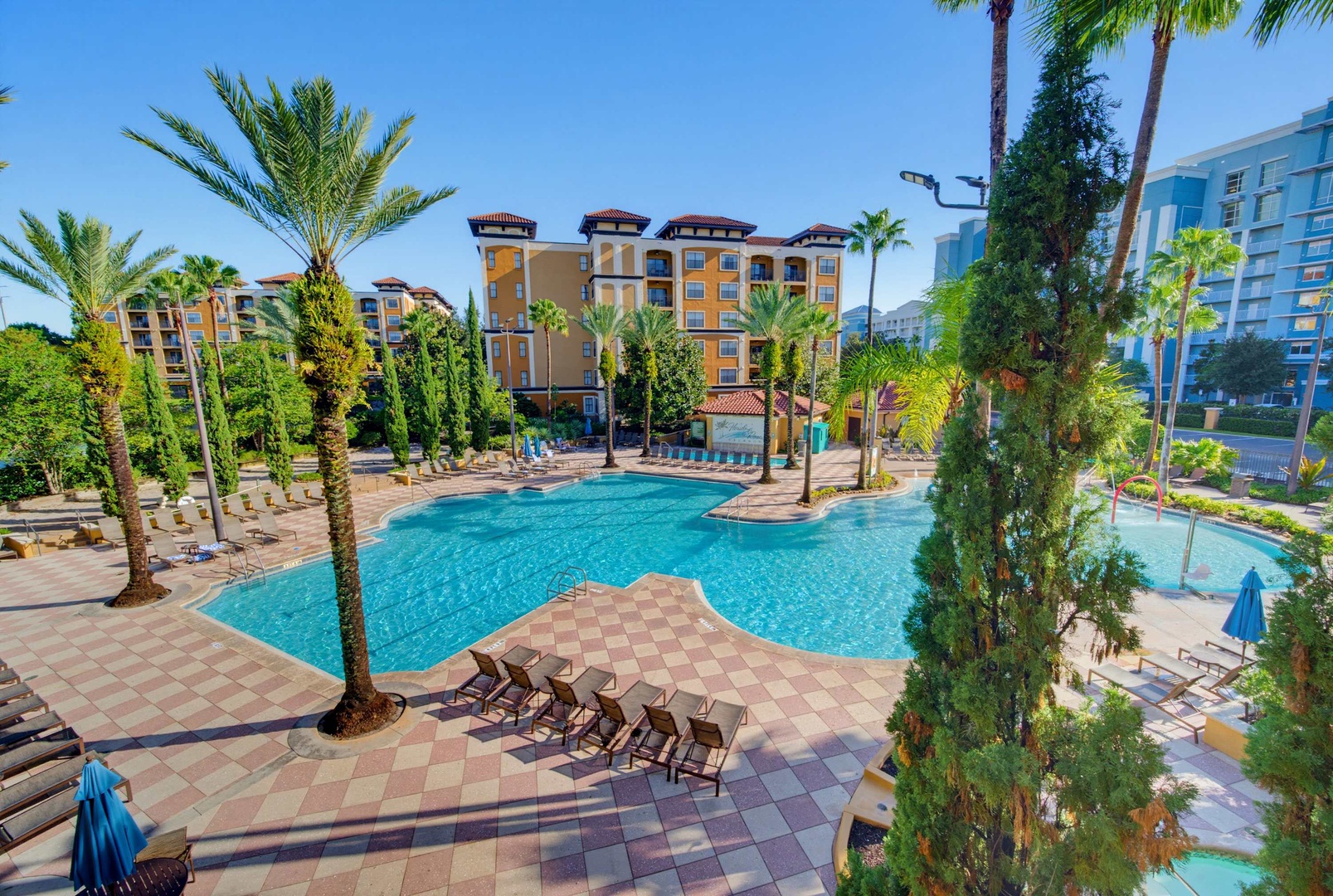 A resort-style pool surrounded by lush palm trees and Mediterranean-inspired architecture creates an inviting oasis for sunny afternoon relaxation.