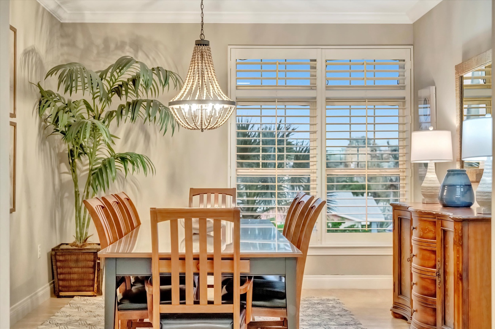 Natural light streams through plantation shutters in this elegant dining space, complete with a chandelier and coastal touches—perfect for morning coffee or evening meals.