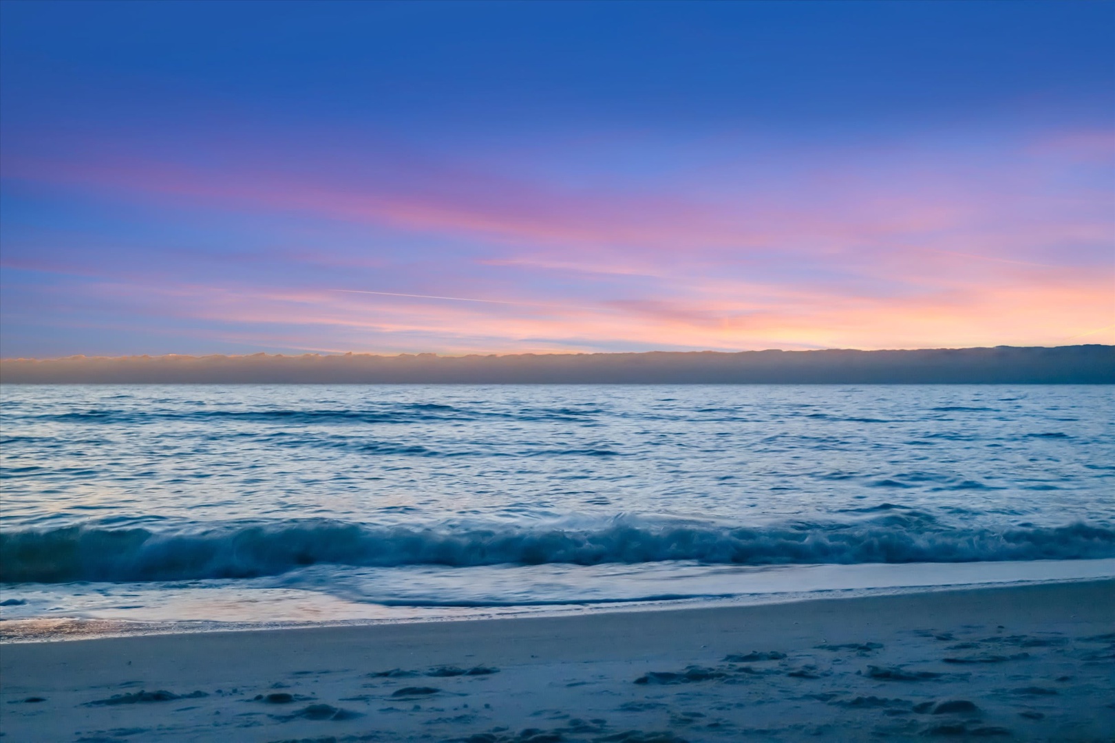 A stunning beachfront location where soft waves meet sandy shores beneath a pastel sky at sunset, just steps from your vacation retreat.