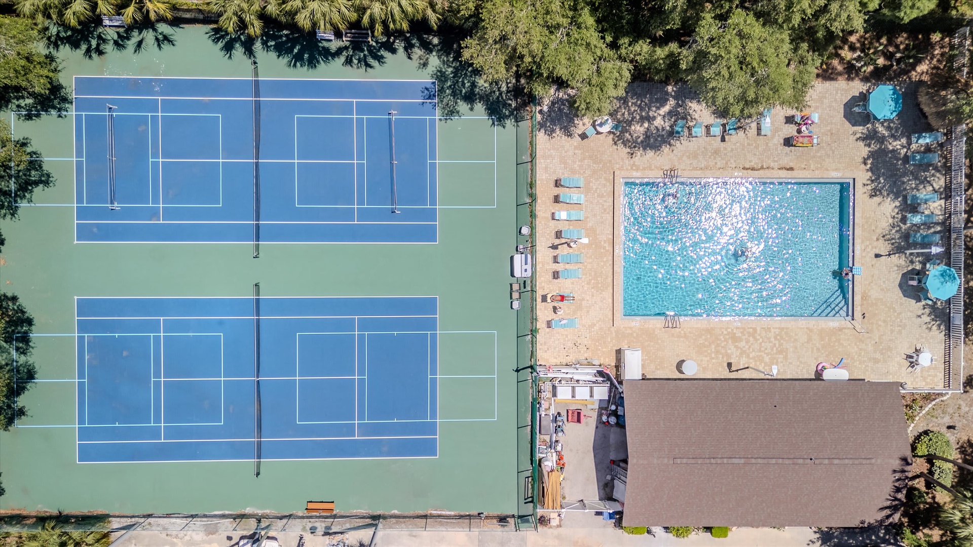 Aerial view of the property's recreational amenities, including tennis courts and a swimming pool surrounded by shaded seating areas.