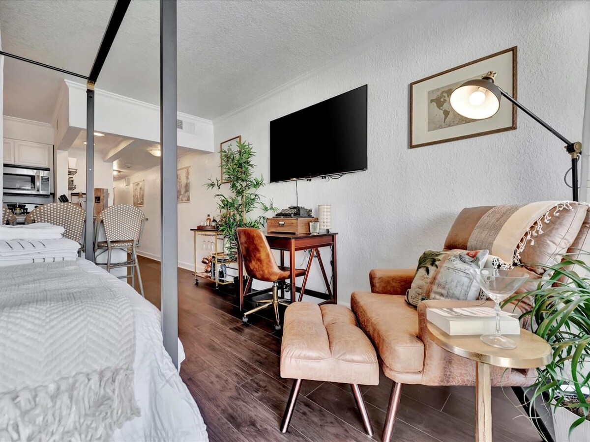 Unwind in your stylish open-concept space where warm wood floors and plush seating create an inviting atmosphere. Stretch out on the velvet lounger, settle into the canopy bed, or catch up on work at the desk—your cozy retreat awaits.