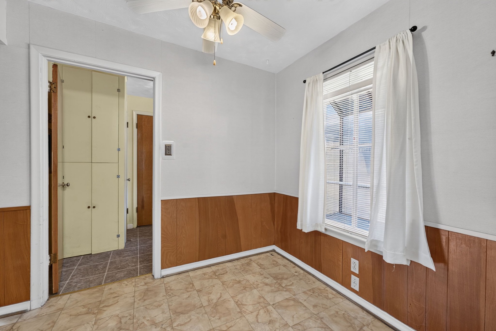 A cozy room featuring charming wood paneling and crisp white walls, bathed in natural light from the window. The adjacent space offers convenient closet storage for all your belongings.