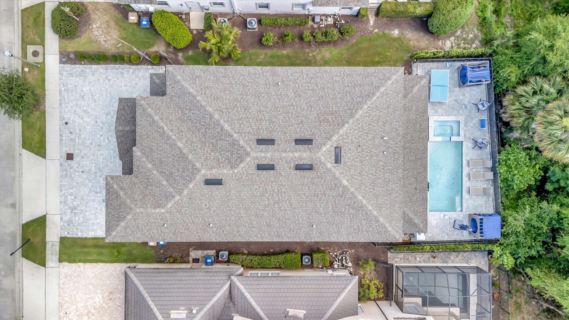 An aerial view captures the property's roofline, showcasing neighboring backyards, a nearby swimming pool, and lush landscaping throughout the residential area.