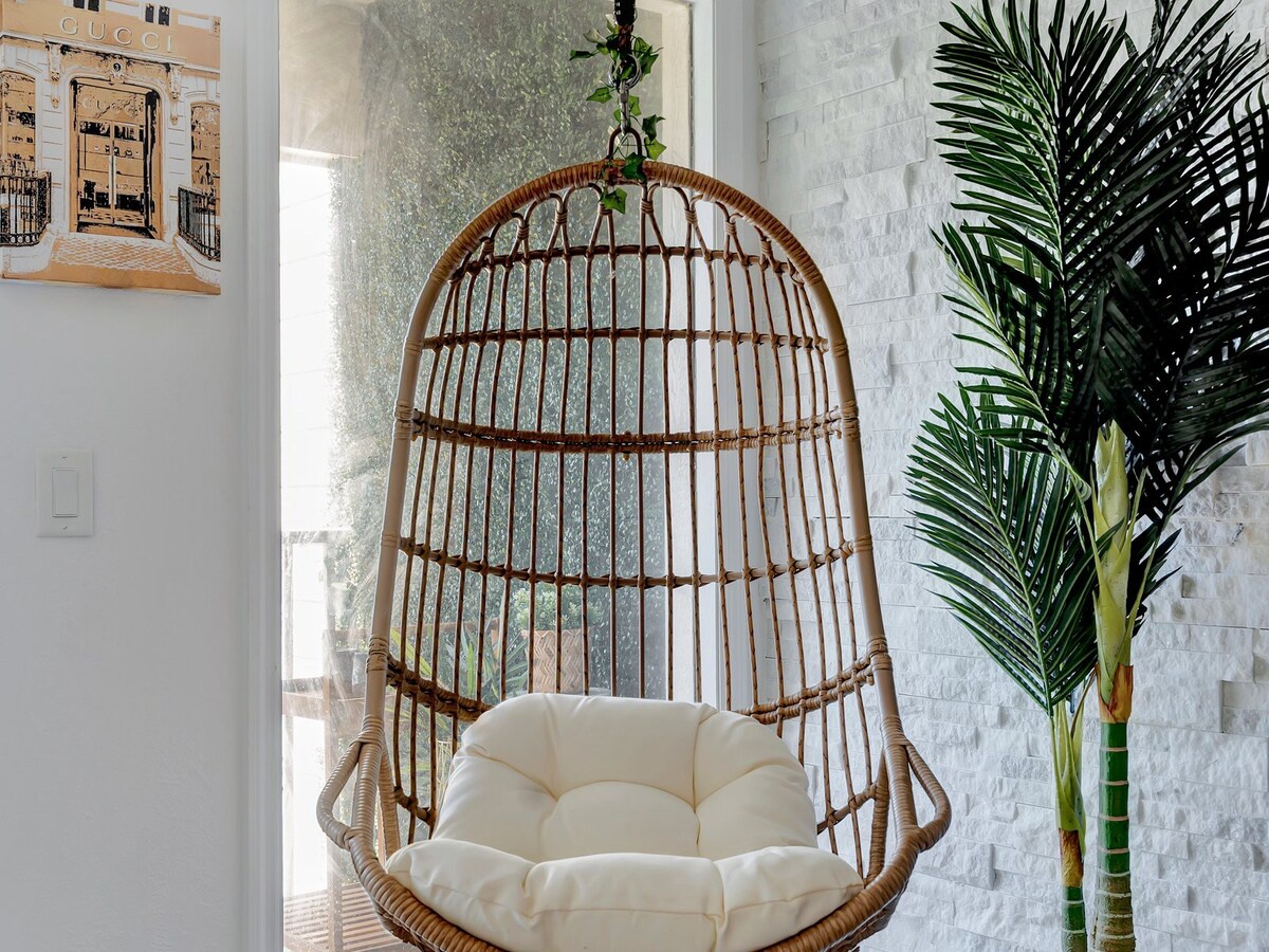 Curl up in your own cozy hanging chair, surrounded by bright white brick and tropical greenery—a perfect nook for morning coffee or afternoon relaxation.