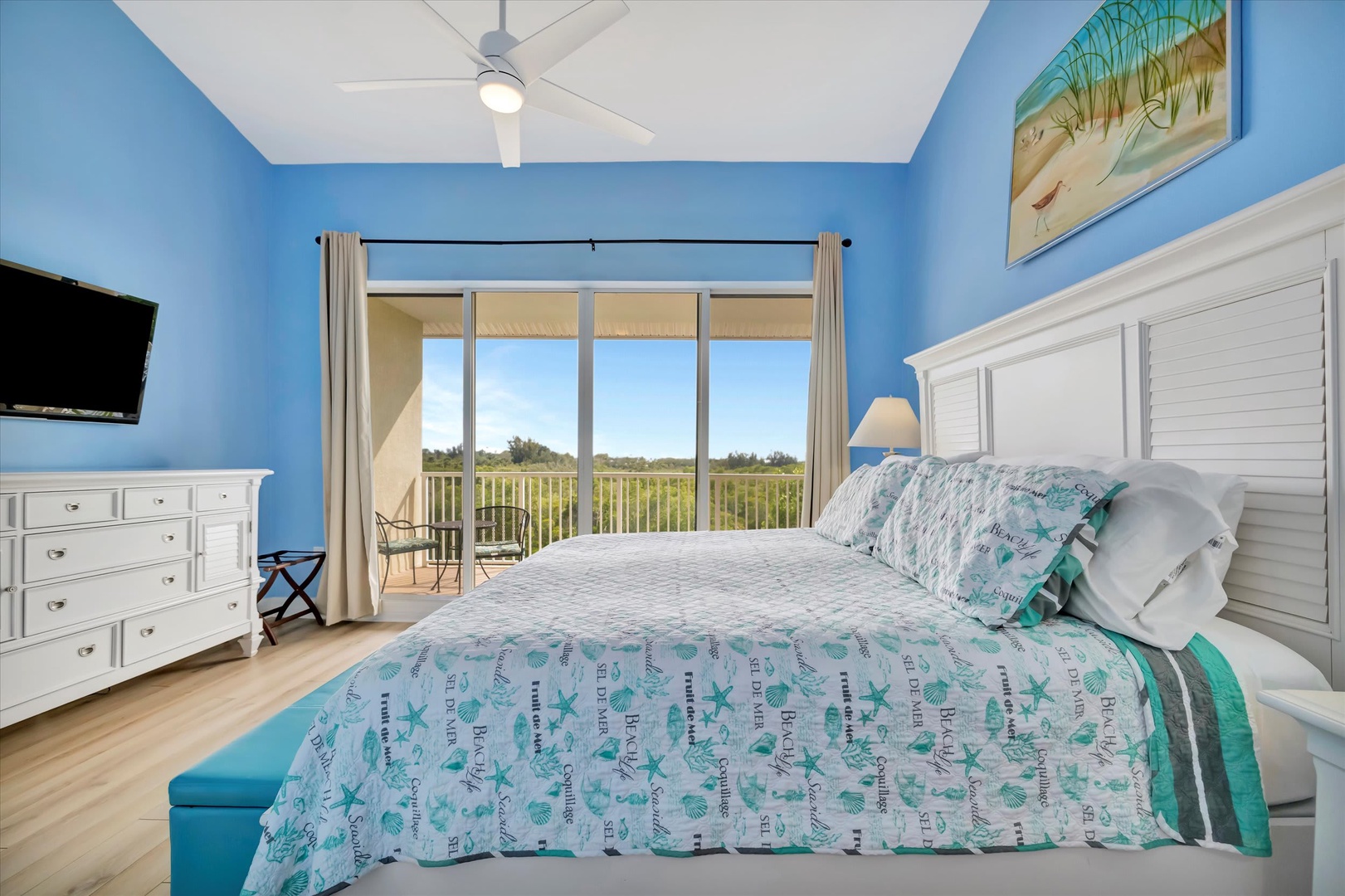 Drift off surrounded by serene coastal colors and natural light, with your own private balcony overlooking lush greenery beyond the glass doors.