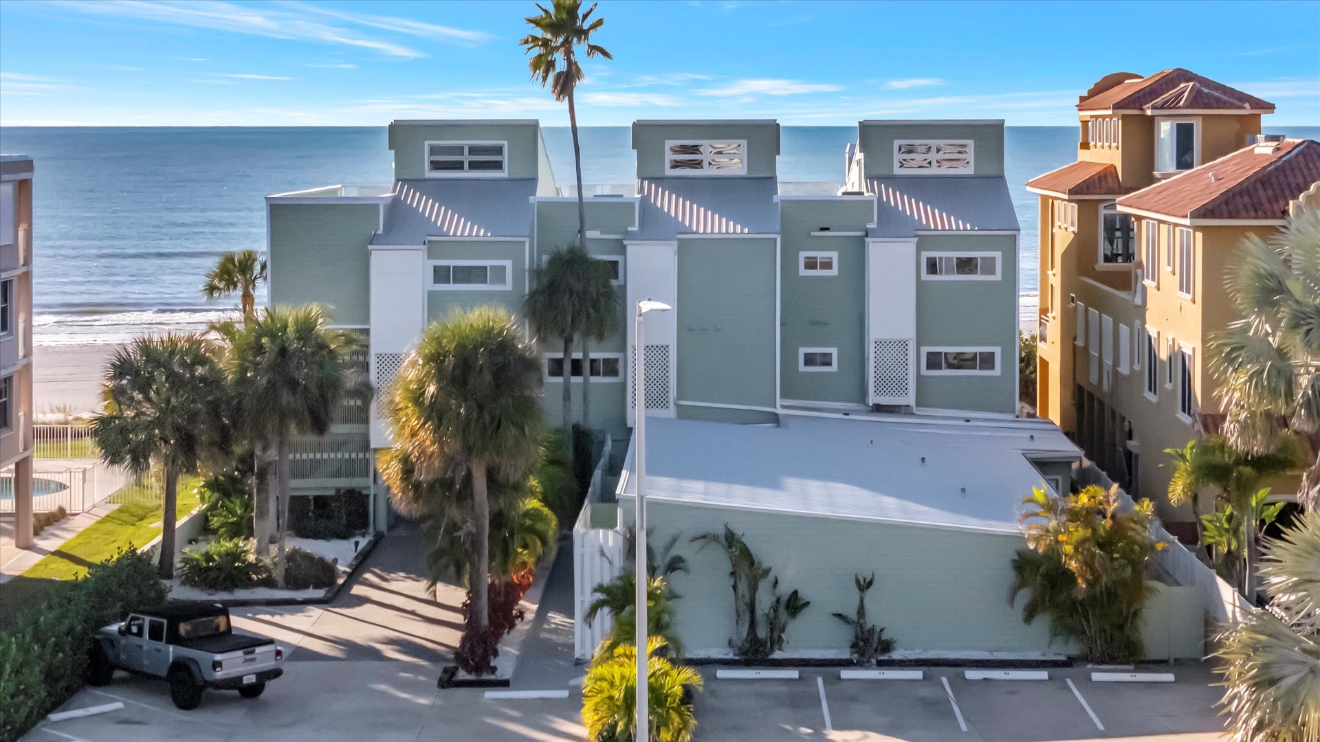 An aerial view of the property nestled among tropical landscaping, with the beach and ocean just steps away. The modern exterior architecture and convenient parking set the stage for your coastal getaway.