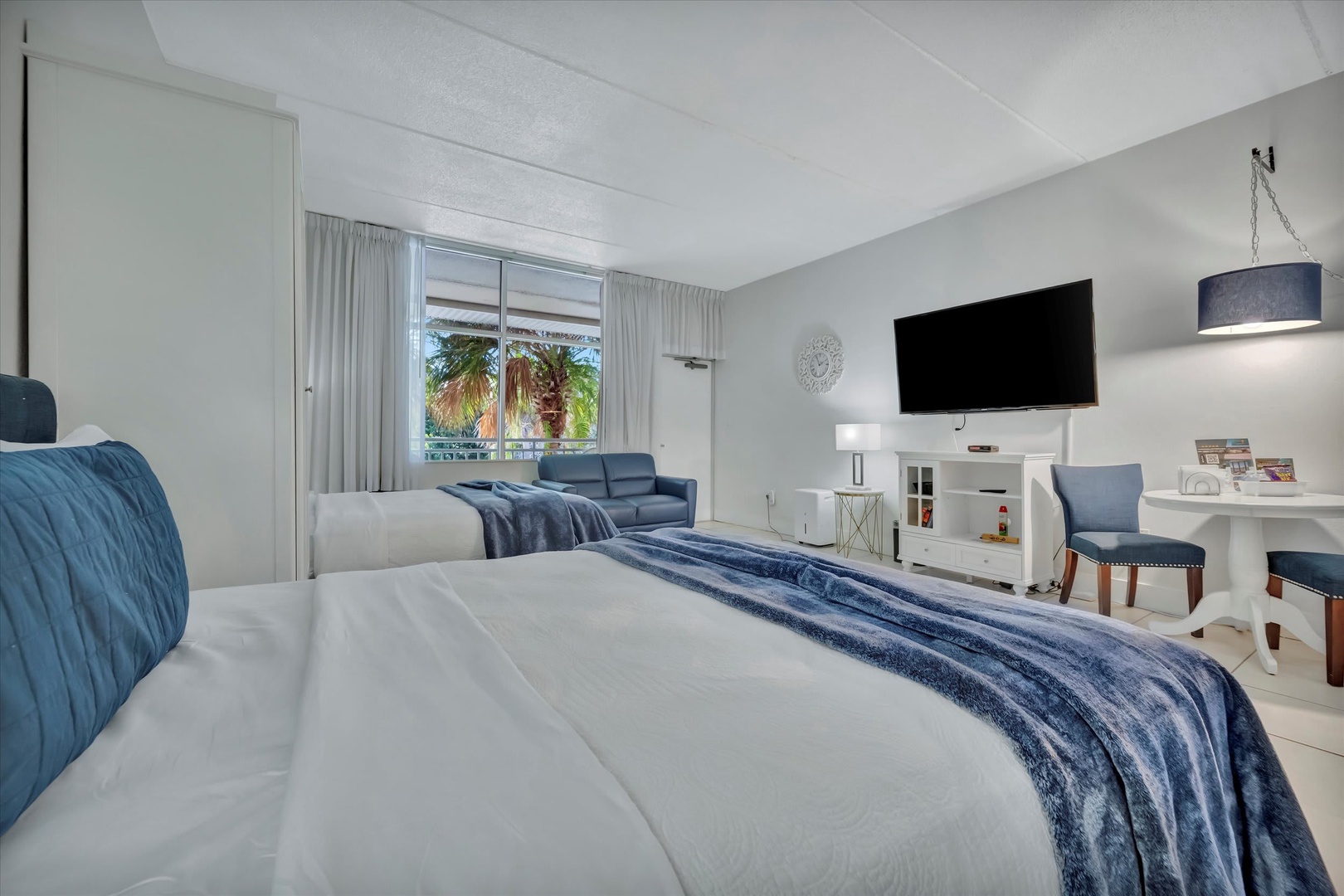 Sink into crisp linens and enjoy your morning coffee with tropical palms framed in the window. A cozy sofa and entertainment setup invite you to unwind in style.