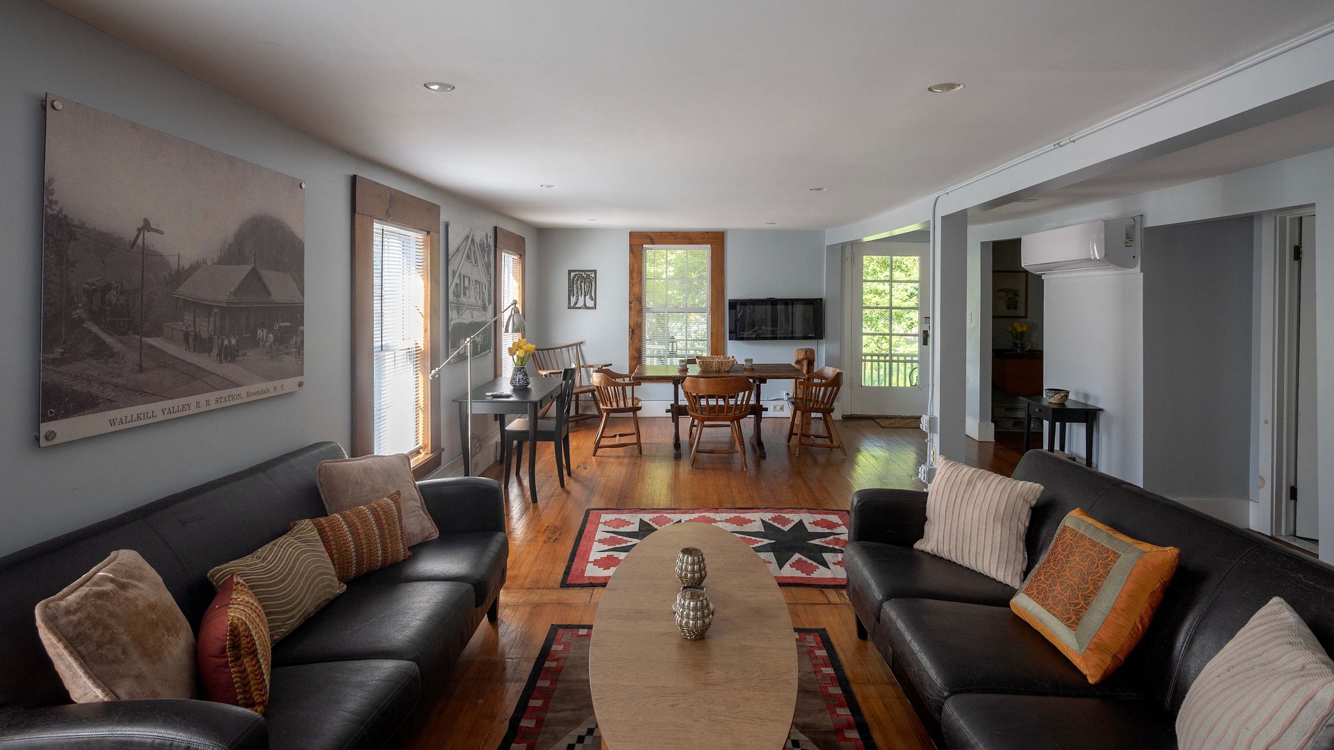 Inviting open-concept living space with rich hardwood floors, sunlit windows, comfortable leather seating, and dining area—your warm, relaxed retreat.