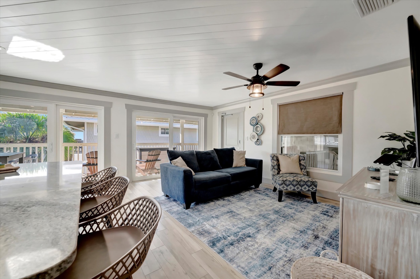 Settle into your bright, airy living space where coastal elegance meets comfort. Relax on plush seating, enjoy the gentle breeze from the ceiling fan, and step through French doors onto your private deck with lush greenery beyond.