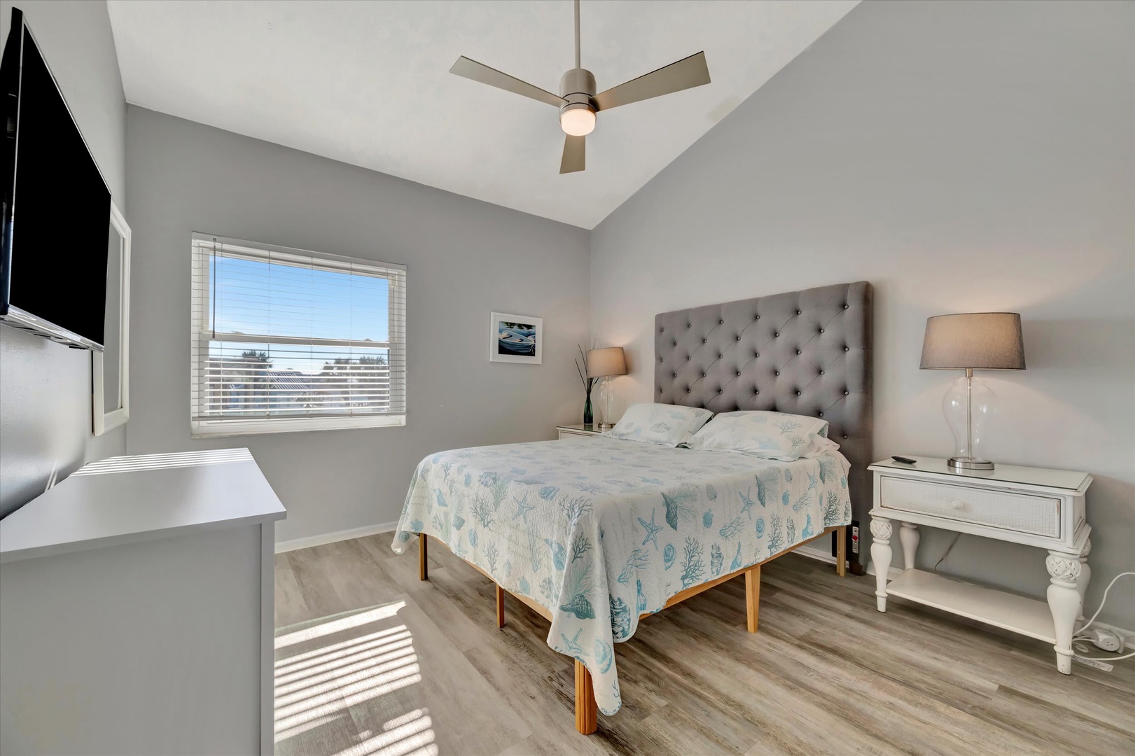 Slip into your peaceful retreat with a plush tufted headboard, soft coastal linens, and a gentle ceiling fan above. Natural light fills your space, inviting relaxation after a day of adventure.