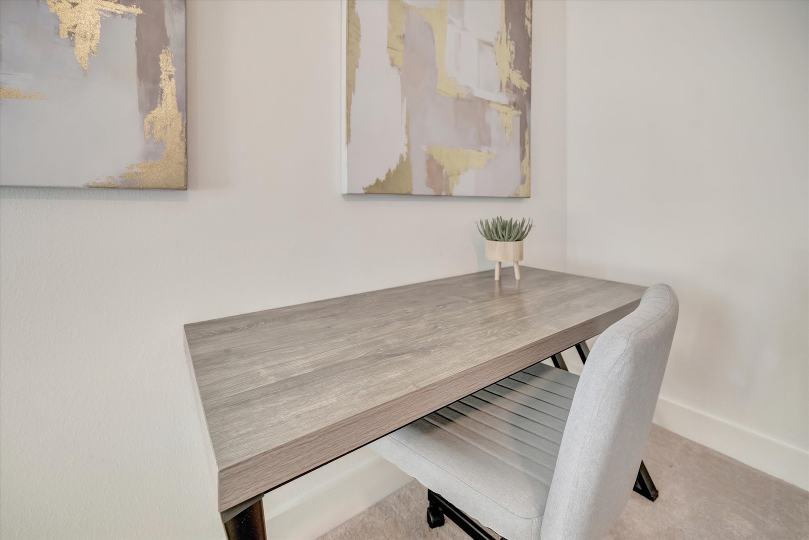 A minimalist workspace awaits your arrival, featuring a sleek wood-toned desk and modern chair beneath elegant artwork. Perfect for catching up on emails or planning your next adventure.