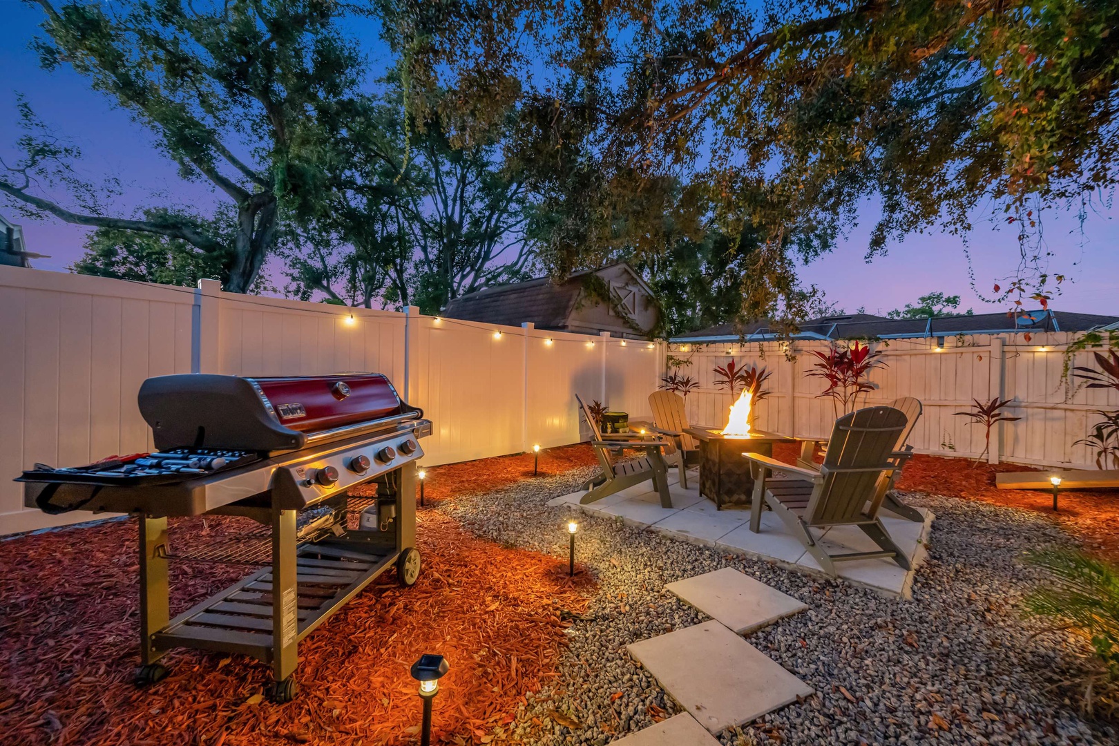 Your private backyard oasis awaits, complete with a glowing fire pit and gas grill, perfect for evening gatherings under twinkling lights and the open sky.
