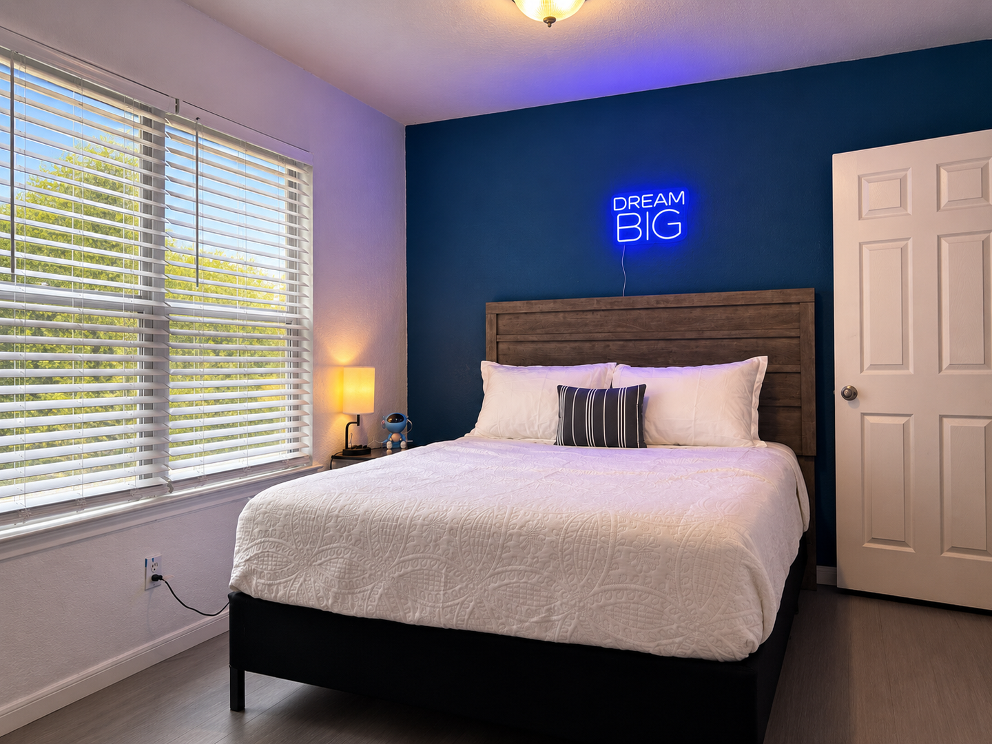 Your cozy bedroom retreat with natural light, plush bedding, and a glowing neon reminder to dream big during your stay.