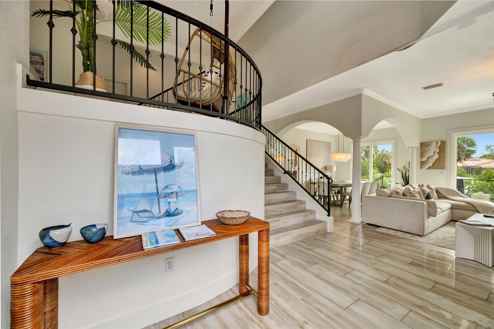 Step into your bright, elegant retreat with soaring ceilings and a stunning curved staircase. Natural light pours through arched windows, illuminating stylish furnishings and warm wood tones—your perfect coastal escape.