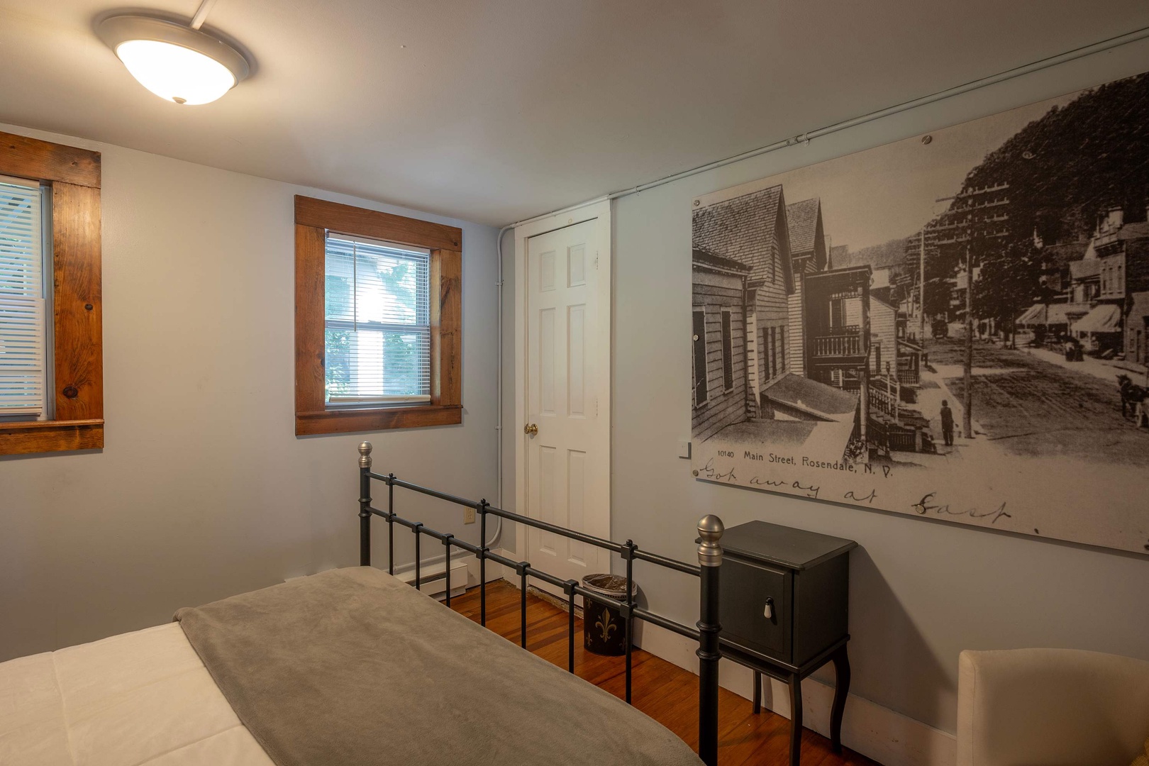Step into your cozy bedroom retreat featuring warm wood accents, gleaming hardwood floors, and charming historic wall art that adds local character to your peaceful getaway space.