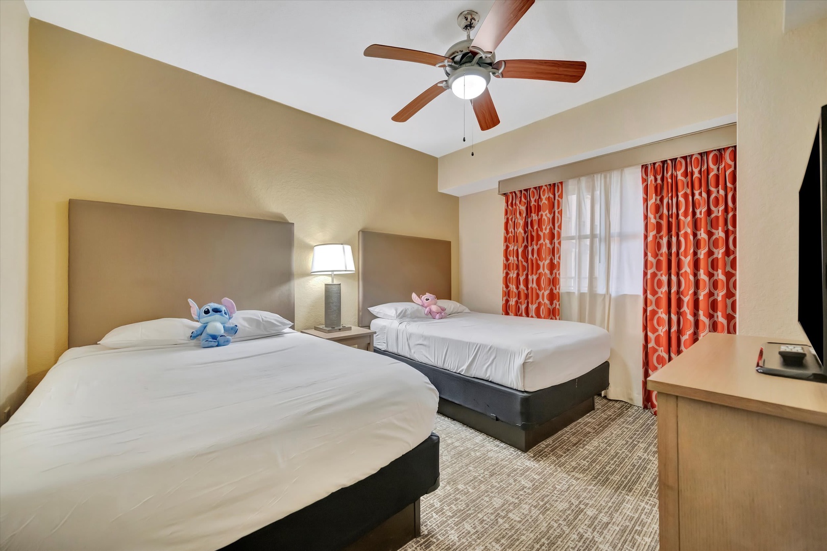 Settle into your bright, comfortable bedroom with two plush beds, a gentle ceiling fan overhead, and cheerful curtains that let in just the right amount of sunlight for a restful retreat.
