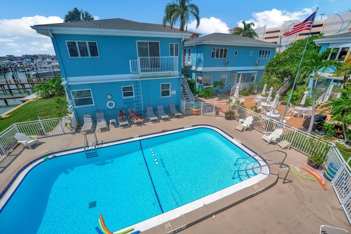 This vibrant blue property offers your perfect coastal escape, with a sparkling pool surrounded by sunny deck space and lounge chairs. Your waterfront retreat sits just steps from the marina, with tropical palms framing your relaxation.