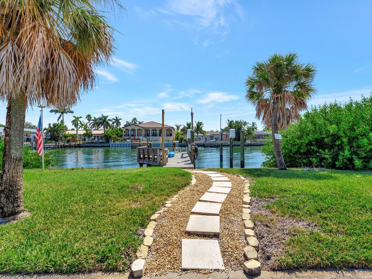 The property features a private waterfront location with direct access to a dock, surrounded by tropical landscaping and scenic canal views in a peaceful residential neighborhood.