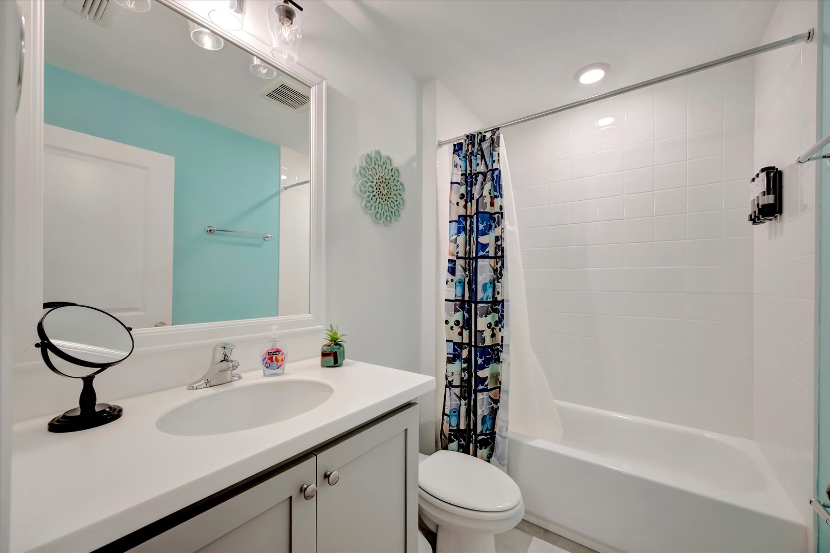 Your private bathroom is fresh and bright, with a full tub-shower combo and crisp white tile. A playful shower curtain and coastal-blue accent wall add a cheerful touch to your daily routine.