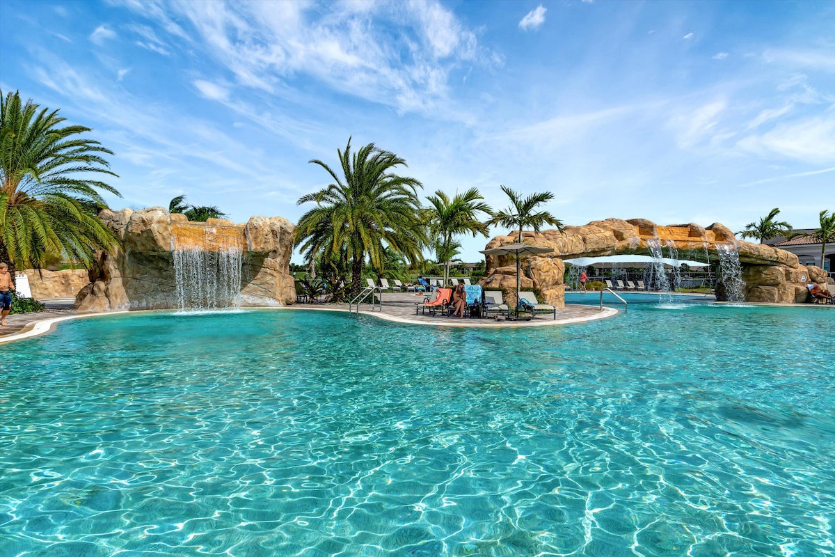 A stunning resort-style pool with cascading waterfalls, tropical palms, and crystal-clear turquoise water invites you to unwind in paradise under sunny skies.