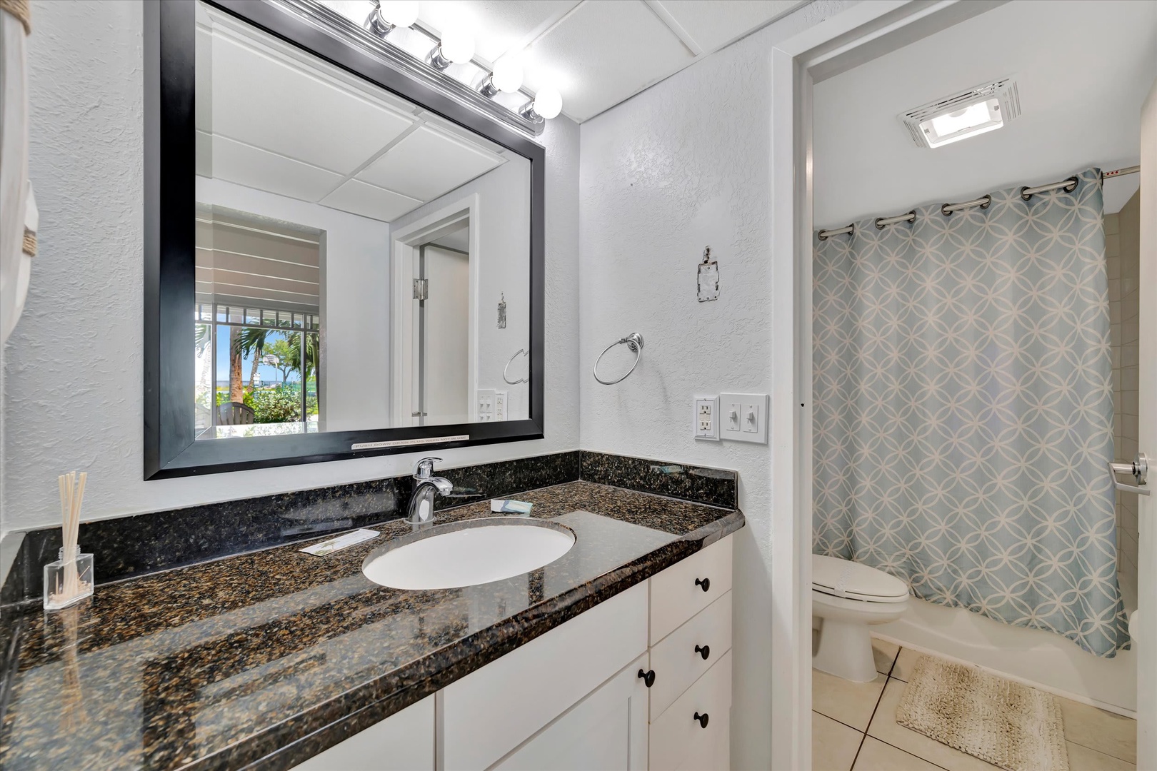Step into your fresh, bright bathroom with granite countertops, a sleek vanity, and a stylish patterned shower curtain. The soft lighting and crisp white tones create a spa-like retreat for your stay.