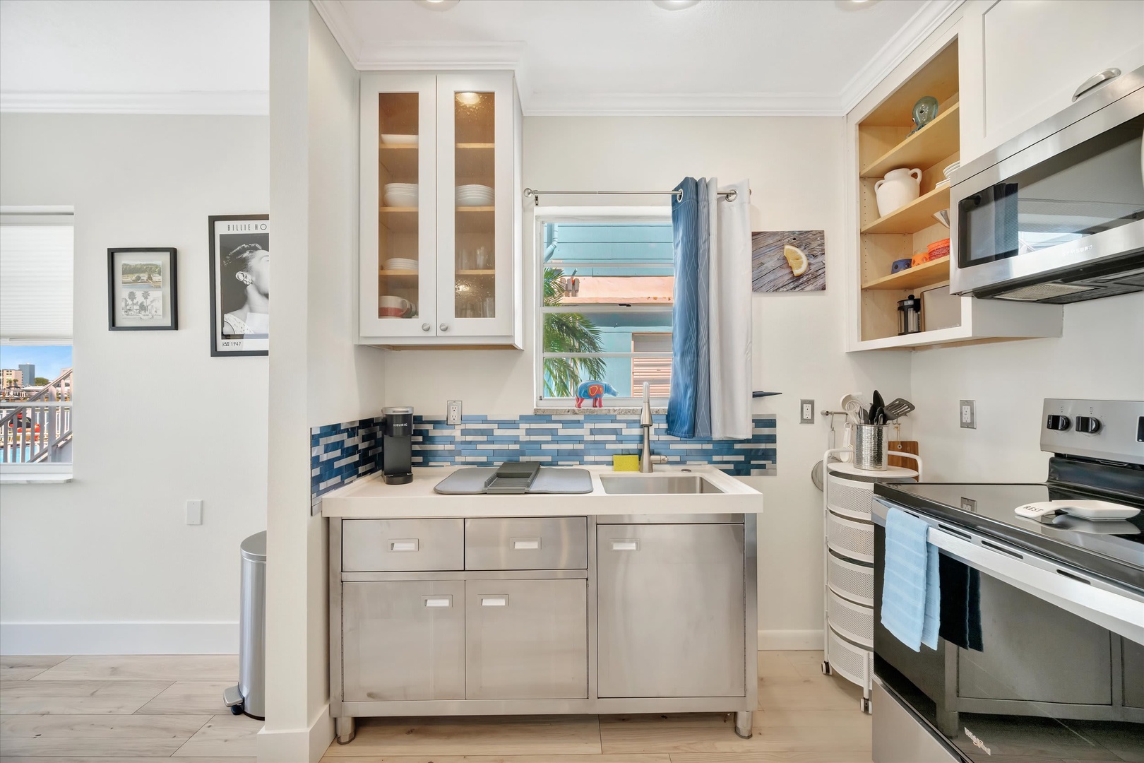 Your fully equipped kitchen features coastal-inspired blue tile and natural light streaming through the window above the sink—perfect for preparing meals while enjoying the sea breeze.
