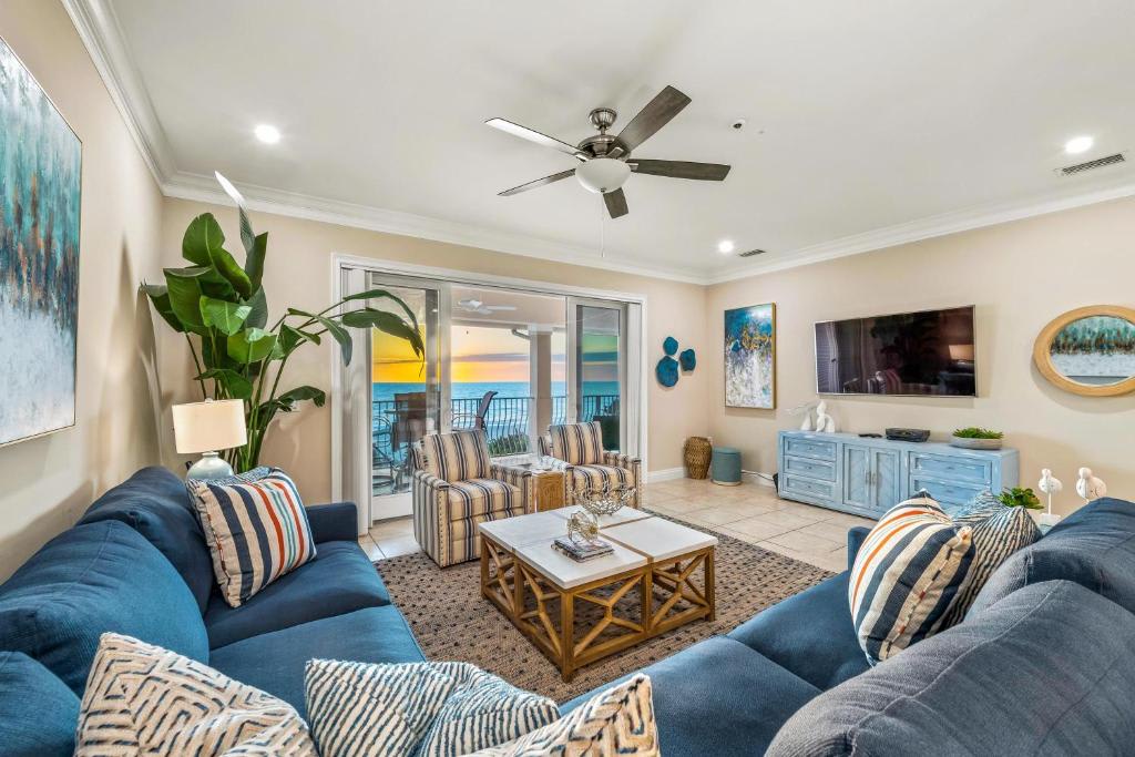 Unwind in your coastal living room with plush sofas, coastal décor, and ceiling fan keeping you cool as sunset paints the sky beyond your private balcony.
