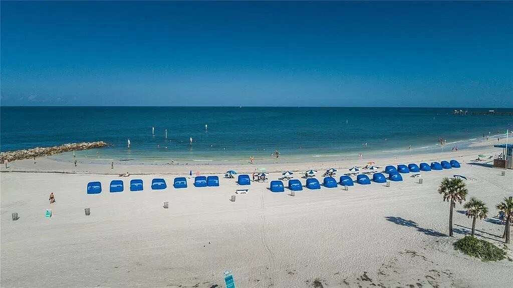 Pristine white sand beach with blue cabanas along the Gulf Coast, offering serene waters and palm-lined shores just steps from the property.