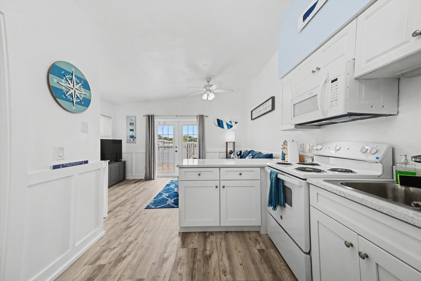 Your bright, breezy coastal retreat features a fully equipped kitchen flowing into a comfortable living space with soft coastal hues, natural light, and balcony access for seamless indoor-outdoor living.