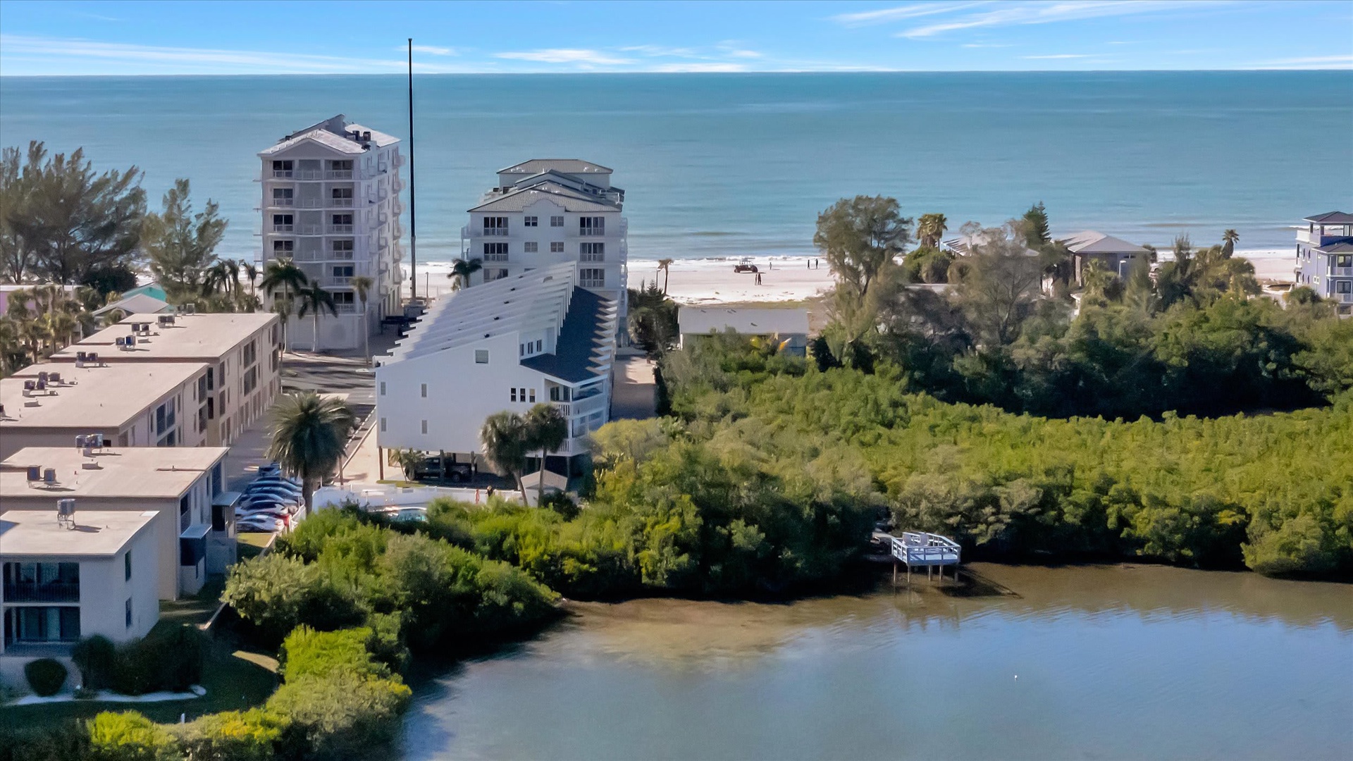 Aerial view of beachfront property nestled between calm intracoastal waters and pristine sandy shores, surrounded by tropical greenery and coastal charm.