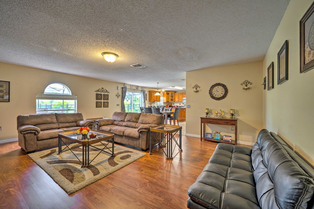 Spacious living area with comfortable sofas, warm wood floors, and natural light from elegant arched windows. The open layout flows seamlessly into the full kitchen.