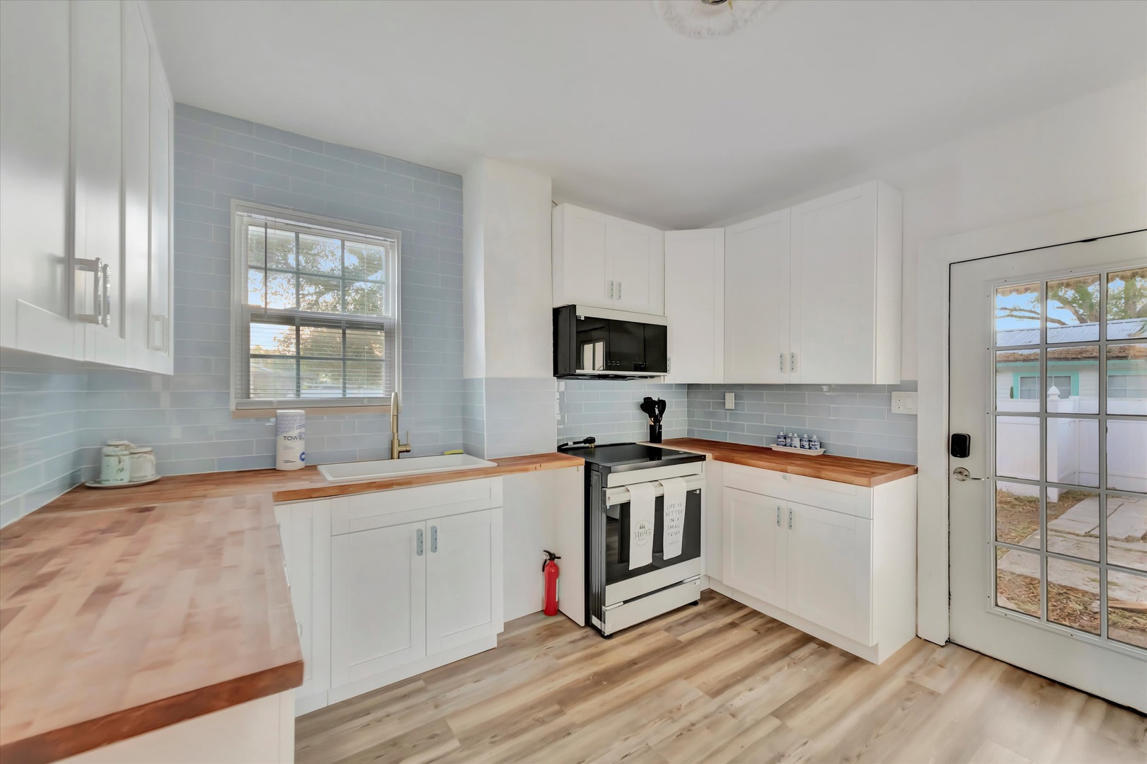 Your bright, coastal-inspired kitchen features warm wood countertops, soft blue backsplash tiles, and crisp white cabinets. Natural light fills the space, making it perfect for morning coffee or preparing meals with loved ones.