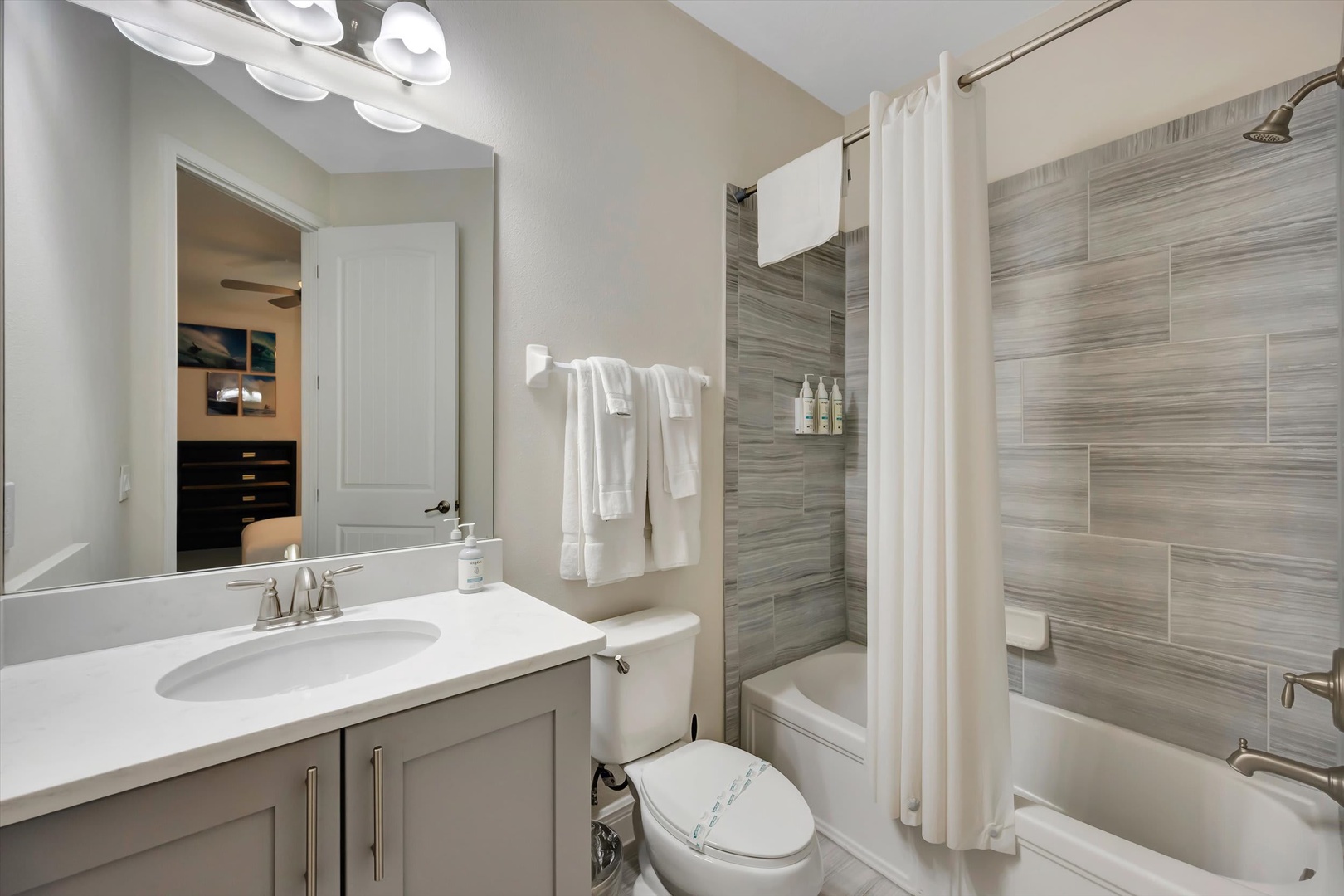 Freshen up in your stylish bathroom featuring elegant wood-grain tile, a spacious tub-shower combo, and crisp white linens waiting for you.