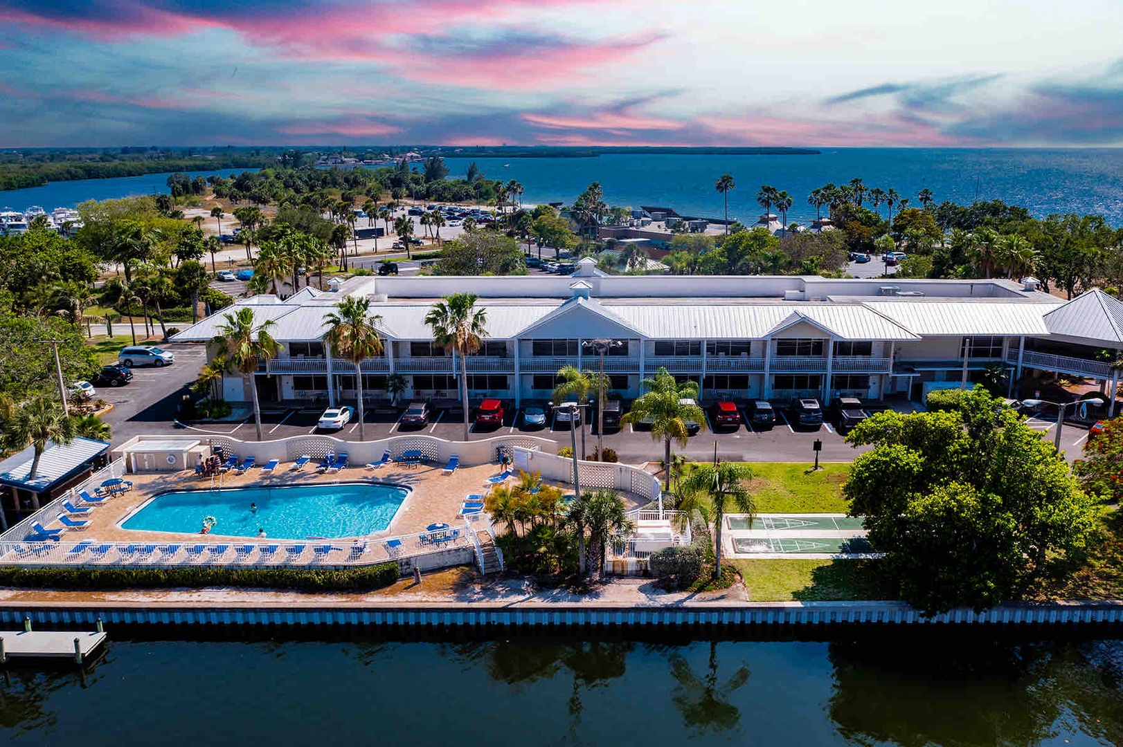Waterfront resort property with swimming pool, tropical landscaping, and direct boat dock access along tranquil bay waters under colorful sunset skies.