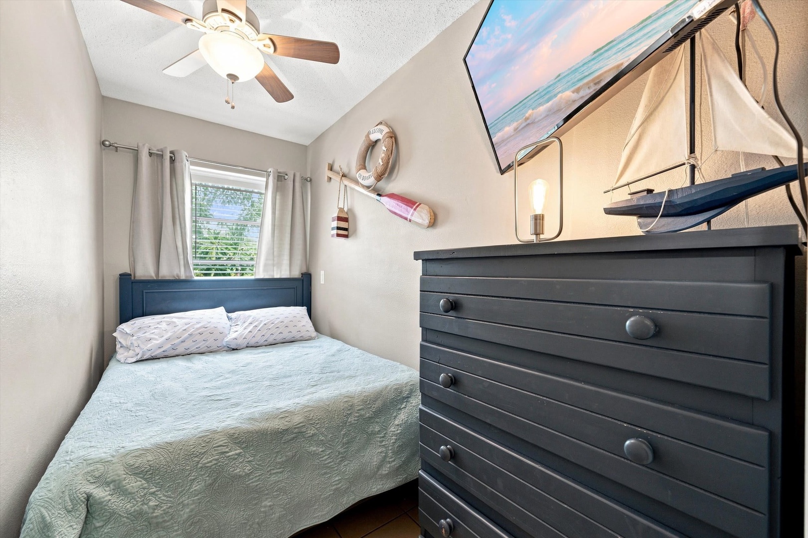 Your coastal-themed bedroom features a comfortable bed, ceiling fan to keep you cool, and nautical touches like the sailboat model and life ring that add seaside charm to the space.
