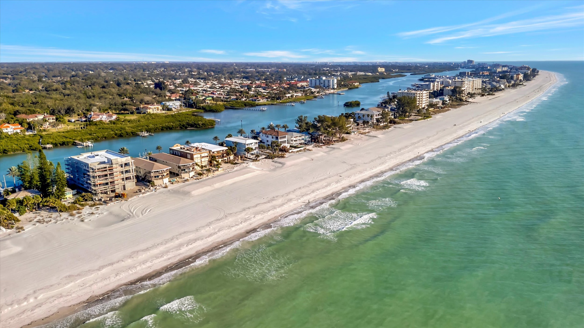 An aerial view of a pristine beachfront community, where soft white sand meets turquoise Gulf waters and a tranquil waterway frames charming coastal homes and resort properties.