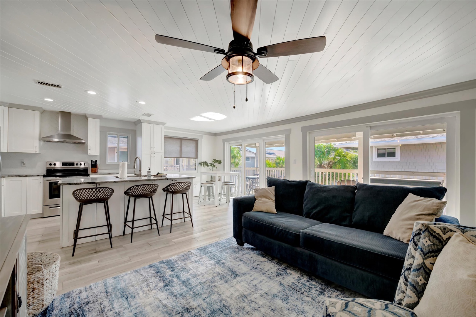 Settle into your open-plan living area where coastal breezes meet modern comfort—plush seating, chef's kitchen, and tropical palms just beyond your windows.
