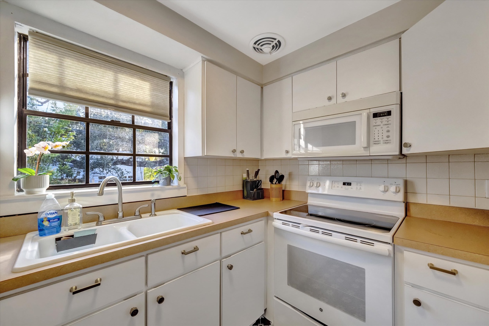 Your well-appointed kitchen features crisp white cabinetry, modern appliances, and a window overlooking lush greenery—perfect for whipping up your favorite meals in a bright, inviting space.