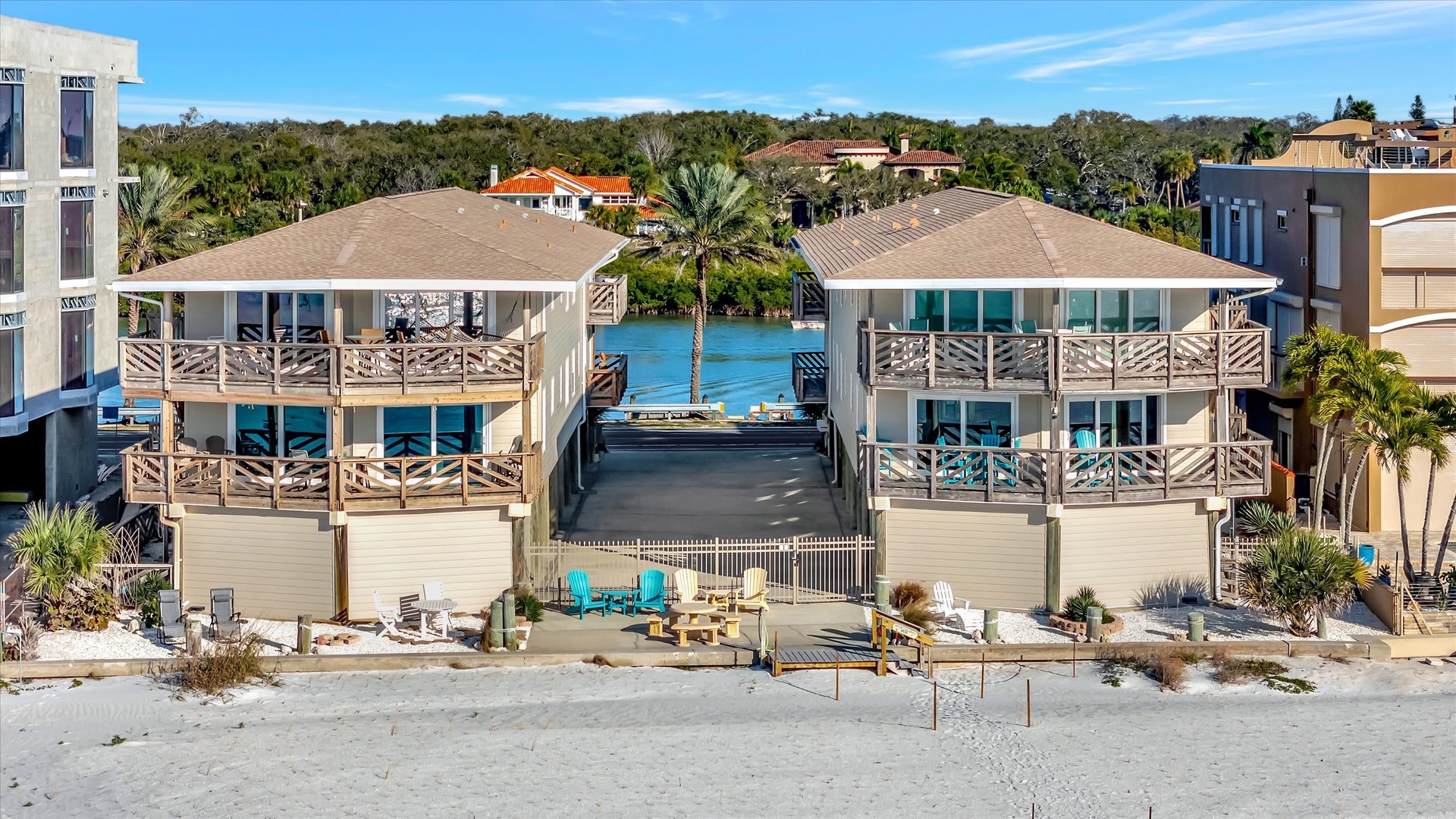 Beachfront duplex property with direct waterfront access, multiple private balconies, and boat docking facilities. Surrounded by lush vegetation and neighboring coastal homes in a tropical setting.