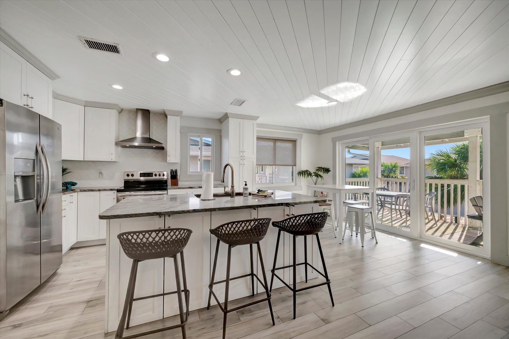 This bright kitchen invites you to gather around the island for morning coffee or casual meals. Step through the glass doors to your private deck and feel the coastal breeze—palms swaying just beyond.