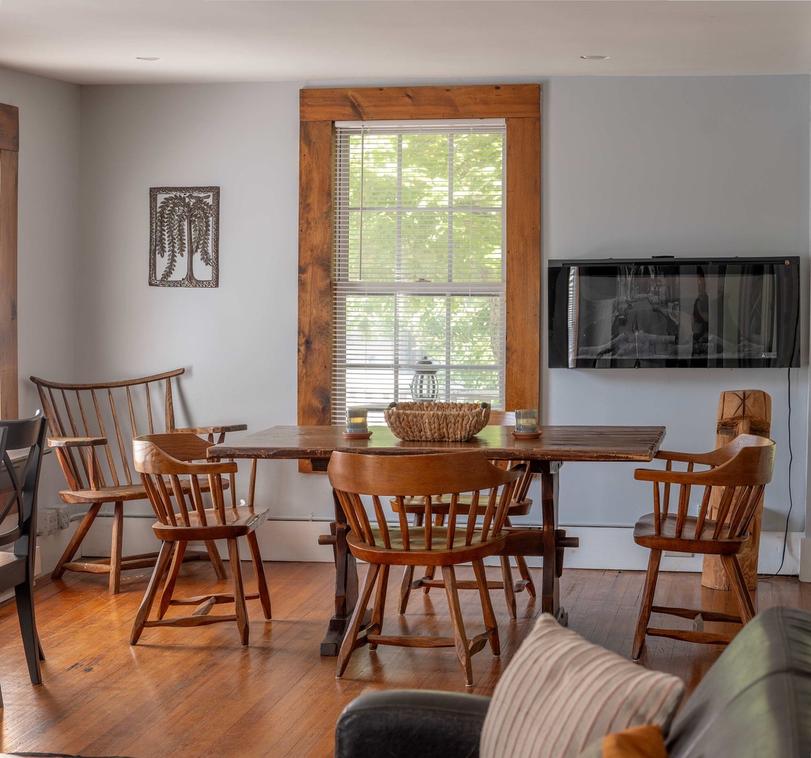 Gather around the handcrafted wooden dining table, where warm morning light streams through the rustic timber-framed window. This inviting space blends farmhouse charm with modern comfort, perfect for your shared meals and conversations.