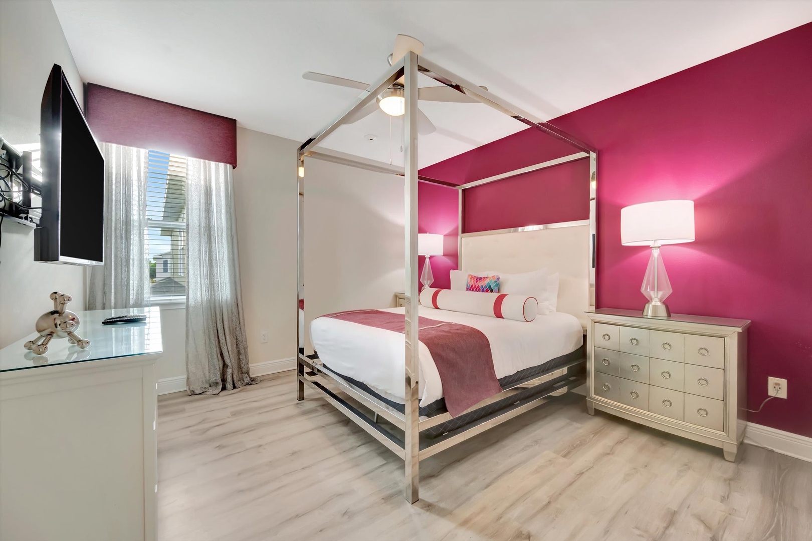 Drift off in your elegant canopy bed, bathed in soft light from modern lamps. Vibrant pink walls add energy and charm, while a flat-screen TV and ample dresser make your stay both stylish and convenient.