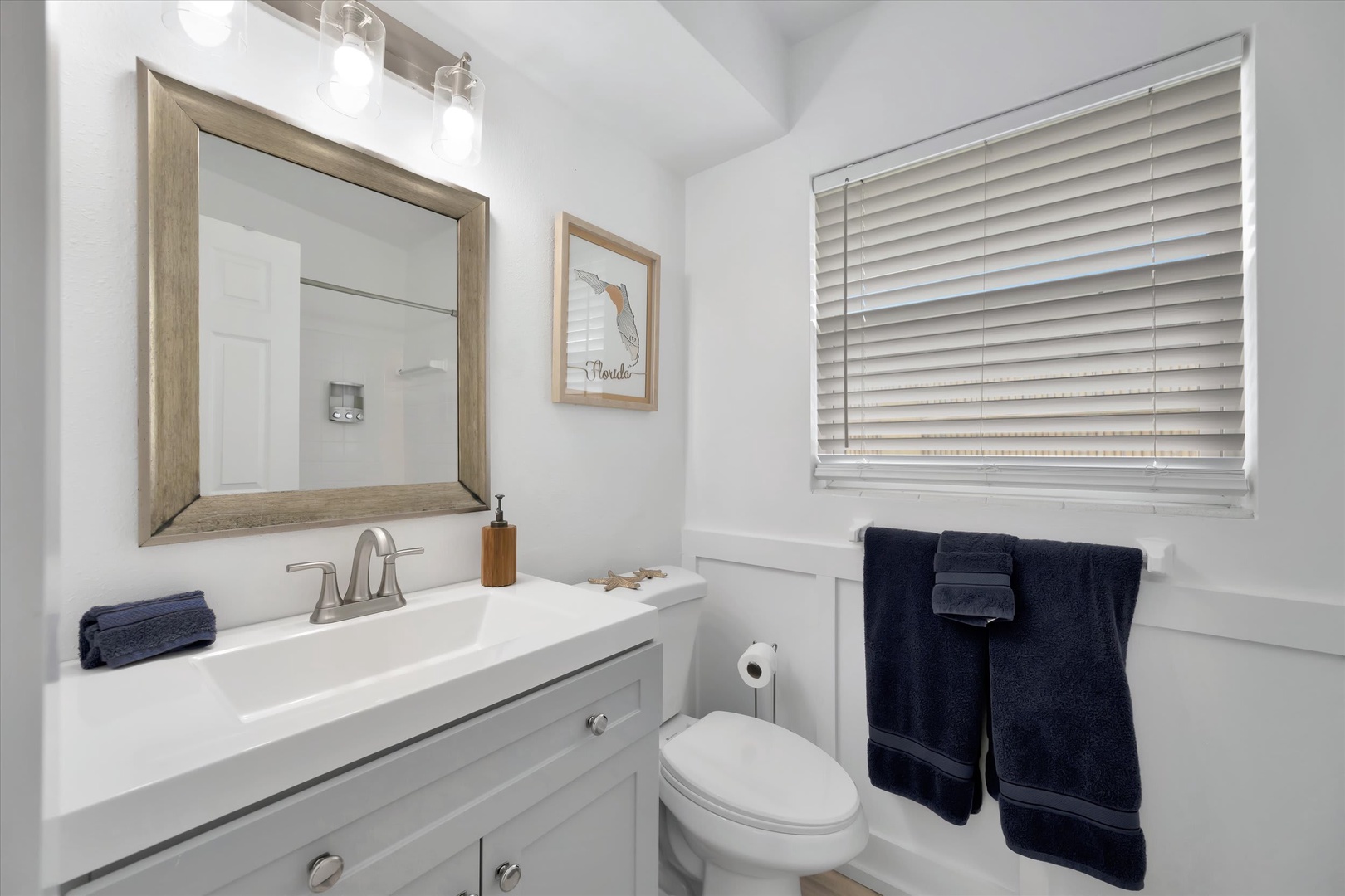 Refresh in this bright, coastal-chic bathroom where crisp white meets warm wood accents and soft navy towels await your arrival.