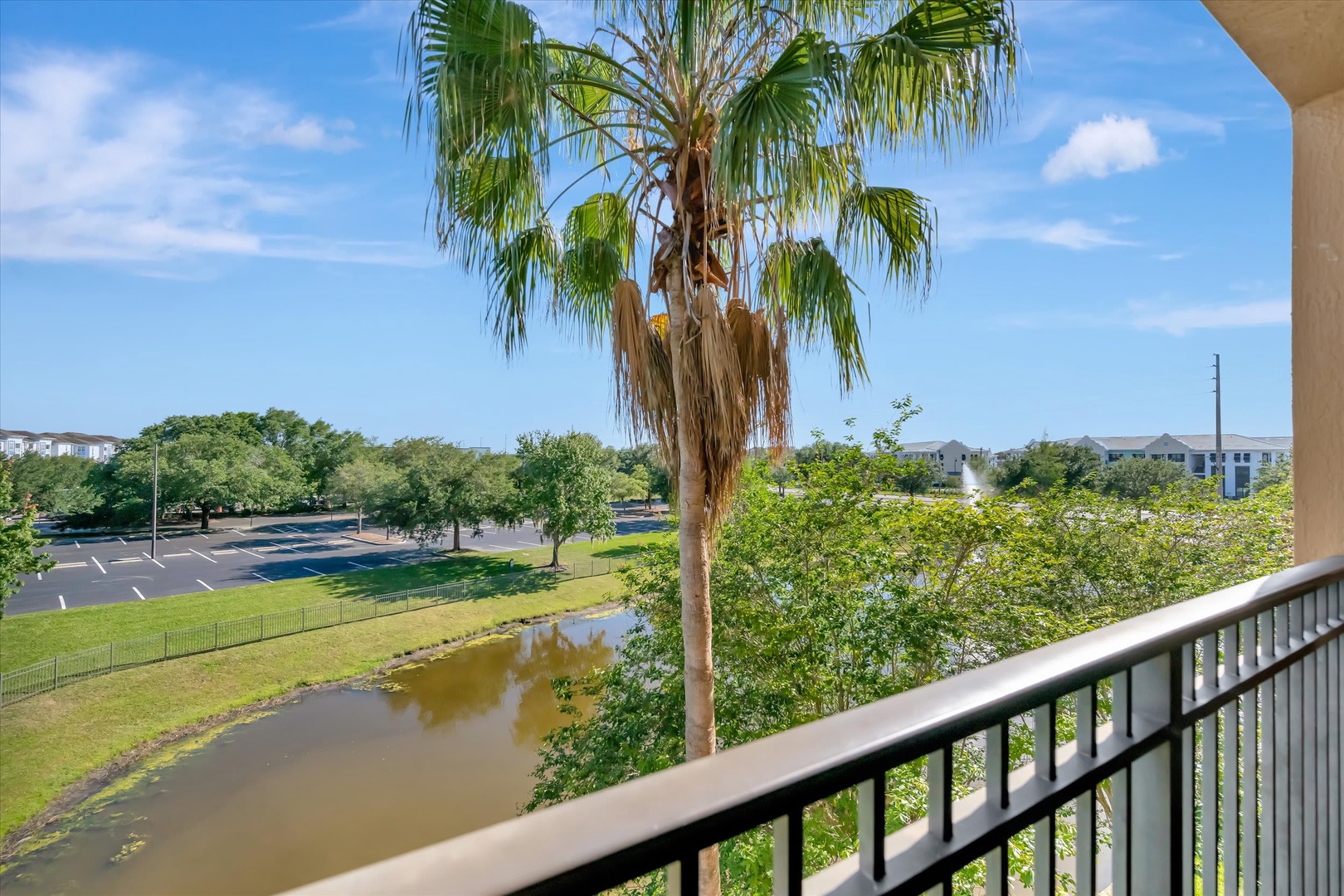 The balcony overlooks a serene pond, green parkland, and scattered palm trees—a peaceful backdrop for morning coffee or evening relaxation in a quiet residential setting.