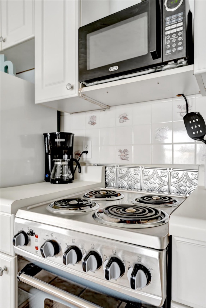 Your fully equipped kitchen is ready for meal prep with a four-burner stove, microwave, and coffee maker waiting to start your day. White cabinetry and gleaming countertops create a clean, welcoming space where you can cook and gather.