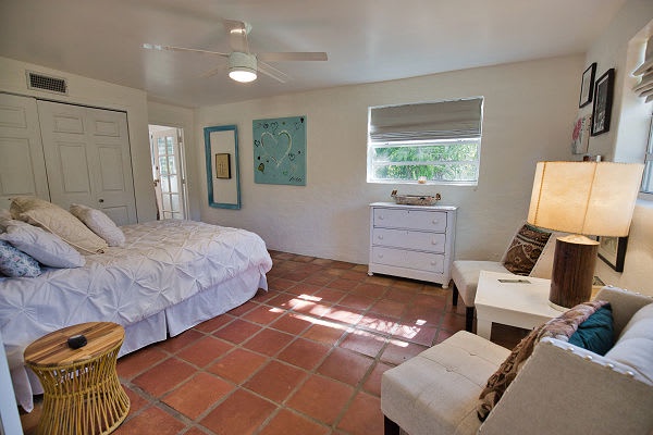 Serene retreat with soft white linens, terra cotta floors, and natural light. Enjoy the ceiling fan and plush bed for ultimate comfort and relaxation.